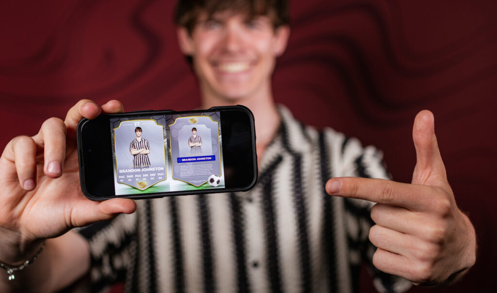 Man in a patterned shirt holding a phone displaying a photo